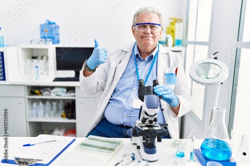 Senior caucasian man working at scientist laboratory doing happy thumbs up gesture with hand. approving expression looking at the camera showing success.