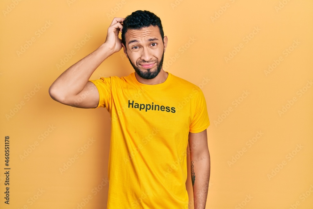 Hispanic man with beard wearing t shirt with happiness word message confuse and wondering about question. uncertain with doubt, thinking with hand on head. pensive concept. Hispanic man with beard wearing t shirt with happiness word message confuse and wondering about question. uncertain with doubt, thinking with hand on head. pensive concept.