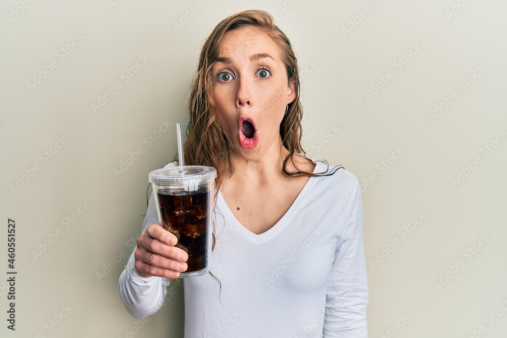 Young blonde woman drinking glass of soda beverage scared and amazed with open mouth for surprise, disbelief face Young blonde woman drinking glass of soda beverage scared and amazed with open mouth for surprise, disbelief face