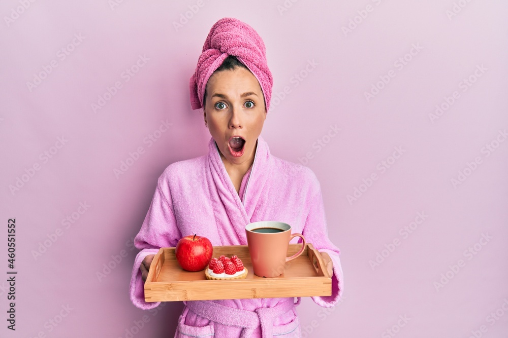 Young blonde woman wearing bathrobe holding tray with breakfast afraid and shocked with surprise and amazed expression, fear and excited face. Young blonde woman wearing bathrobe holding tray with breakfast afraid and shocked with surprise and amazed expression, fear and excited face.
