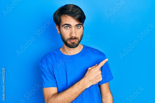 Young hispanic man wearing casual clothes pointing with hand finger to the side showing advertisement, serious and calm face