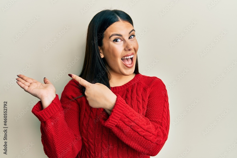 Beautiful brunette woman wearing wool winter sweater amazed and smiling to the camera while presenting with hand and pointing with finger. Beautiful brunette woman wearing wool winter sweater amazed and smiling to the camera while presenting with hand and pointing with finger.
