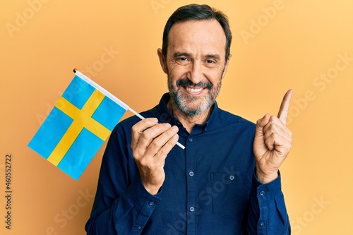 Middle age hispanic man holding sweden flag smiling happy pointing with hand and finger to the side photo