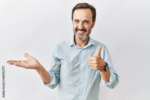 Middle age hispanic man with beard standing over isolated background showing palm hand and doing ok gesture with thumbs up, smiling happy and cheerful