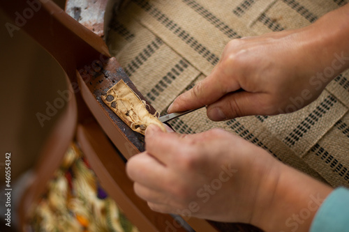 A close up of upholsterer's hands removing antique upholstery nails. Restoration of an antique chair.