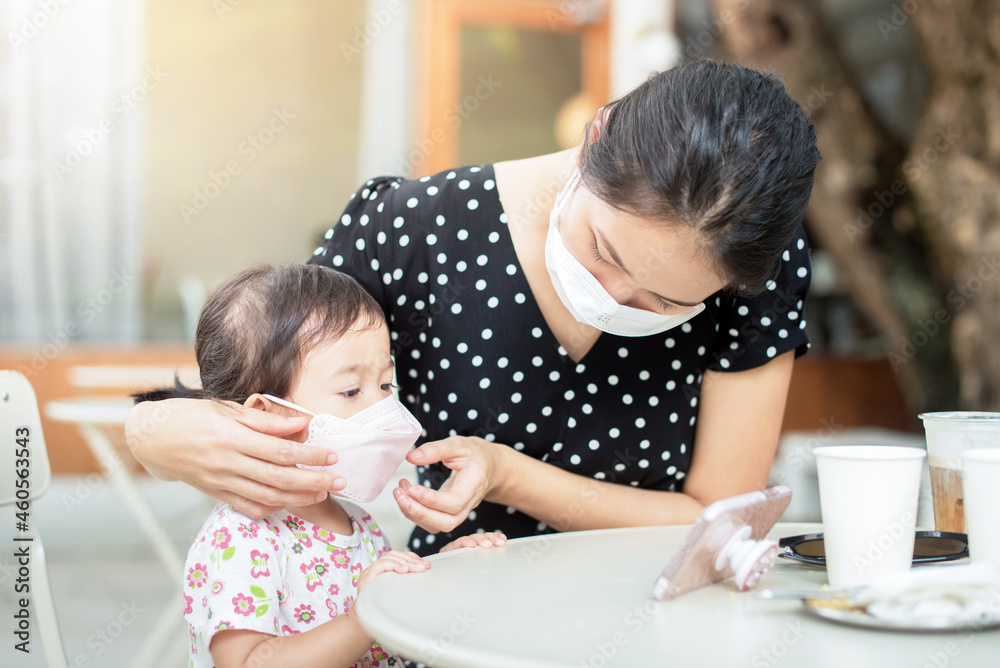 Young mother putting on mask to her baby daughter on the lunch table in garden Young mother putting on mask to her baby daughter on the lunch table in garden