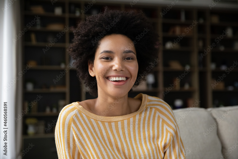 Happy young african american woman sitting on couch, looking at camera, enjoying video call meeting with friends. Professional biracial female blogger streaming in social network online, webcam view. - obrazy, fototapety, plakaty 