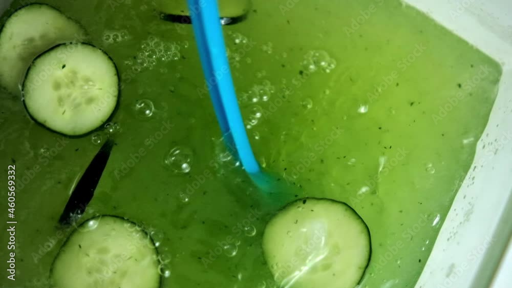 Blue ladle stirring refreshing cucumber drink in slow motion