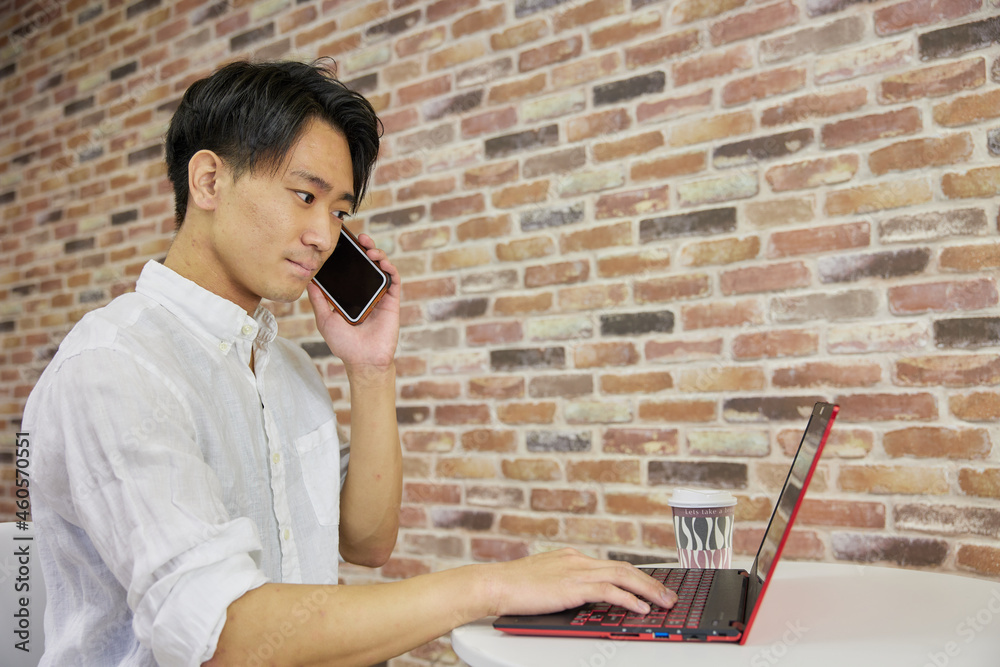 電話しながらノートパソコンを触る日本人男性