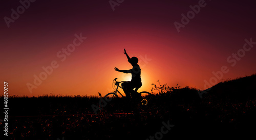 Balance, Enjoying Life and Harmony Concept. Silhouette of Happiness Person on Bicycle with raised arms to Balancing Body during Sunrise or Sunset
