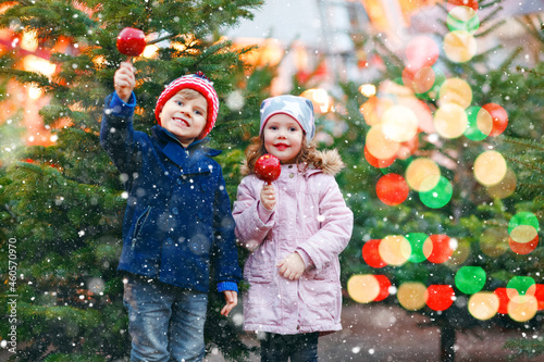 Two little smiling kids, preschool boy and girl eat sweet sugared apple on German Christmas market. Happy siblings children with lights on background and xmas trees. Family funny brother and sister. photo