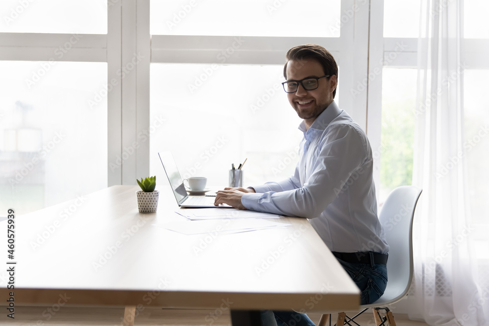 Portrait smiling businessman in glasses sitting at desk with laptop home office workplace, working online, happy successful man entrepreneur freelancer looking at camera, posing for picture