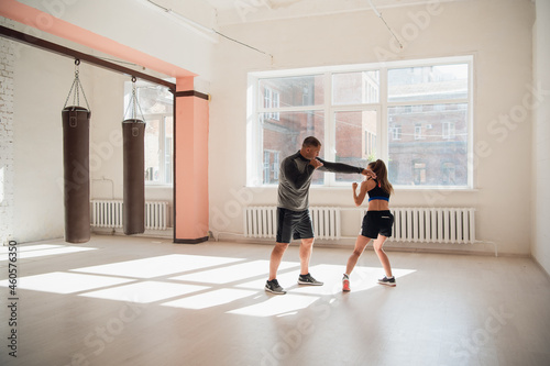 Female boxer practicing hits with her personal trainer in a boxing studio.