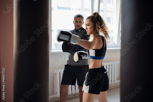 Beautiful woman boxing combat bag with sport trainer together. Girl boxer exercising box punch with personal coach. © romankosolapov