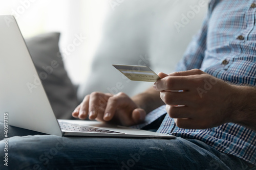 Crop close up man purchasing goods or paying domestic bills online by credit card, using laptop, typing entering information, young male customer making secure internet payment, shopping at home