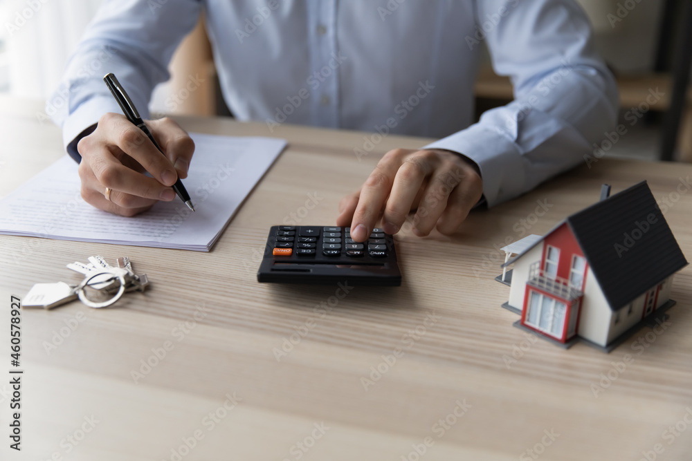 Fototapeta premium Businessman realtor using calculator, sitting at desk with house mockup and keys close up, calculating mortgage rate, preparing documents for contract signing, real estate purchasing concept