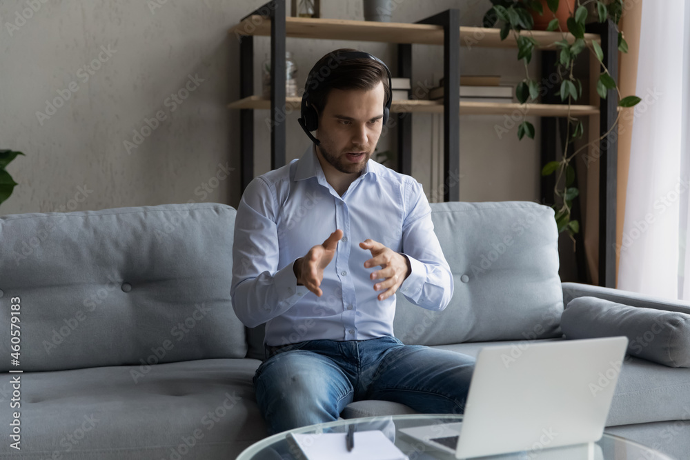 Confident man in wireless headset talking, consulting client, working online at home, serious businessman looking at laptop screen, engaged in internet meeting, conference, teacher leading webinar Confident man in wireless headset talking, consulting client, working online at home, serious businessman looking at laptop screen, engaged in internet meeting, conference, teacher leading webinar