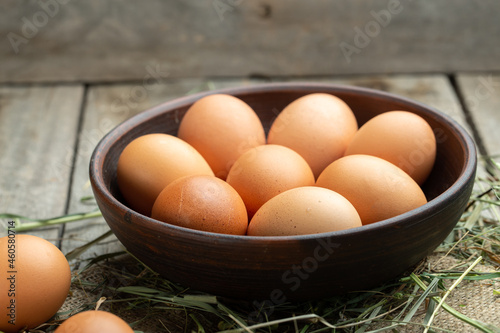Chicken eggs in a clay bowl on a wooden background, hay scattered around. Healthy food concept.