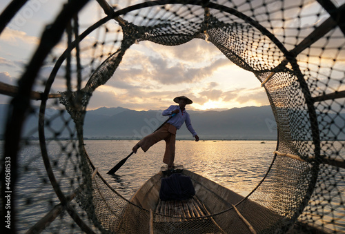 view through fish coop of local fisherman standing on boat in lake at sunrise