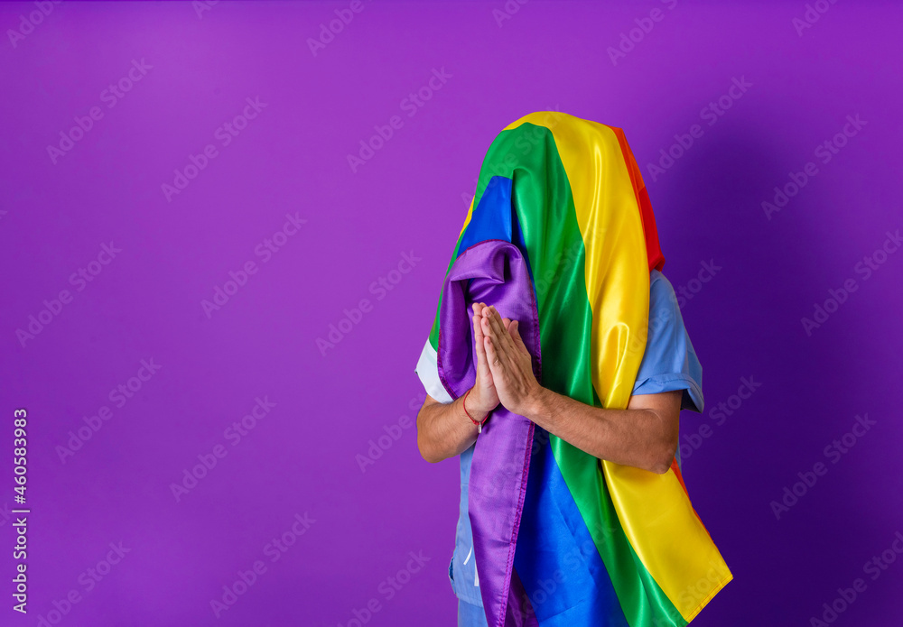 Fototapeta premium Unrecognizable person with LGBT flag covering his head. Gay pride concept. Purple background with copy space.