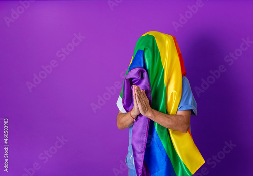 Unrecognizable person with LGBT flag covering his head. Gay pride concept. Purple background with copy space.