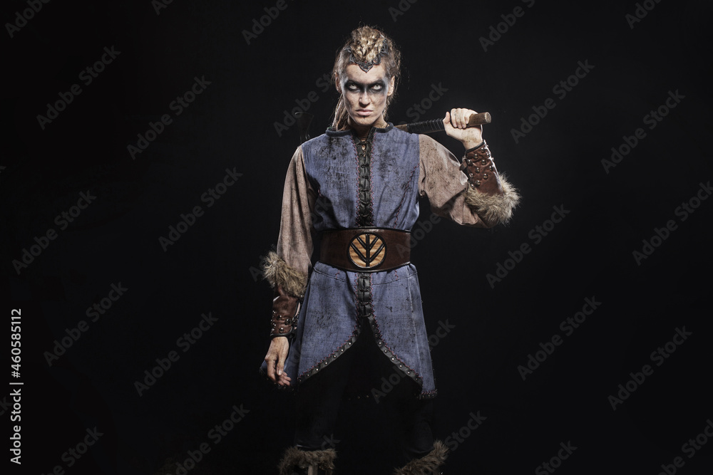 Woman viking warrior in history costume with ax on dark background