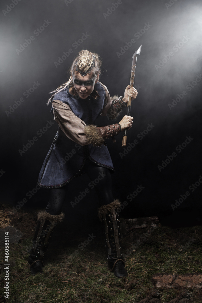 Woman viking warrior in history costume with ax aggressively attacks on dark background