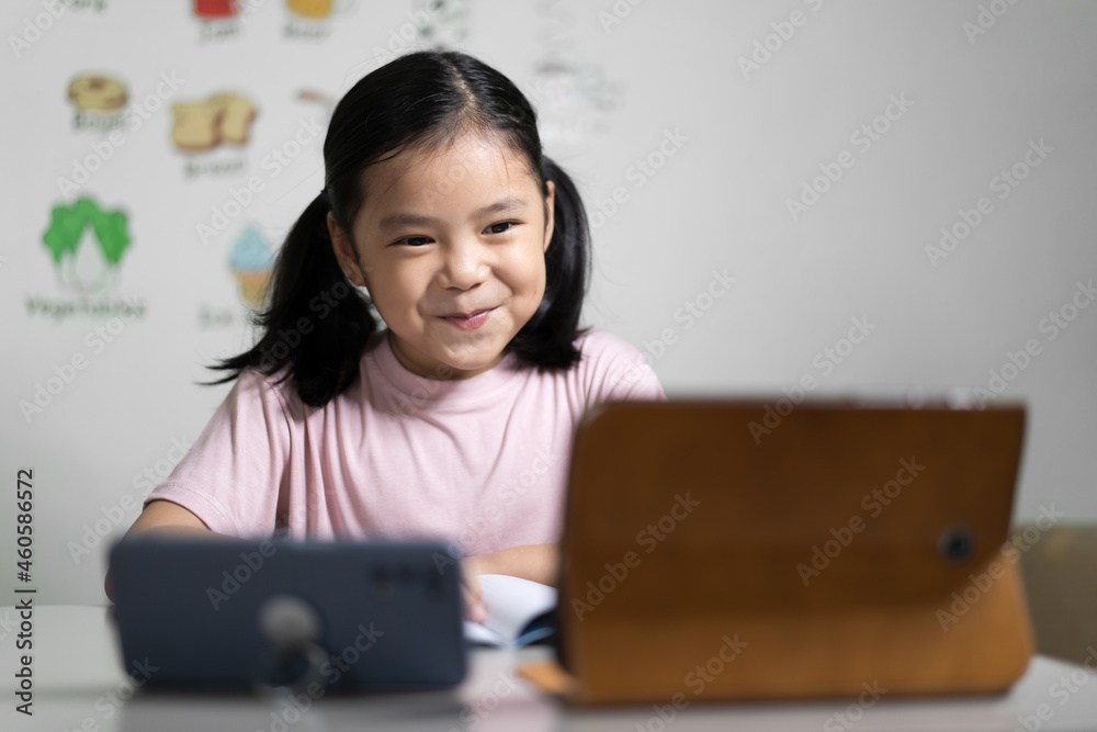 Asian child student learning on computer tablet or kid girl smiling learn from home school or person study online and video call on smartphone with happy enjoy to vocabulary english words in classroom Asian child student learning on computer tablet or kid girl smiling learn from home school or person study online and video call on smartphone with happy enjoy to vocabulary english words in classroom