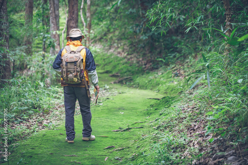 travel man with backpack and holding map walking on green forest trail.