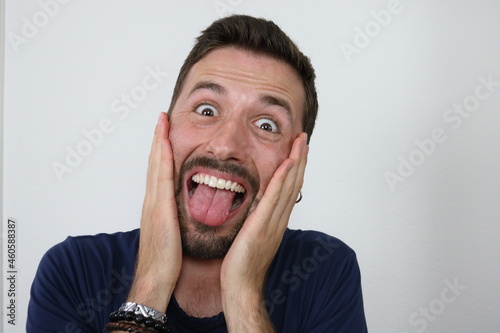 Young attractive caucasian Man showing his tongue and touching his face with both hands. 