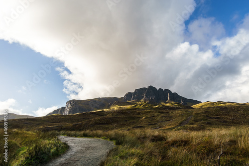 path leading to the Old Man of Storr at golden hour with dark rock formation in background, Isle of Skye, Scotland