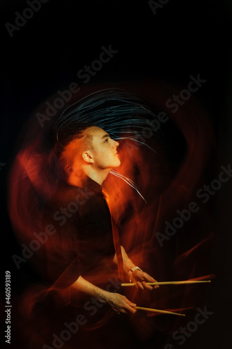 Handsome man with interesting braids on a black background with drumsticks, shot with mixed light