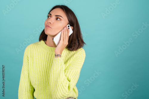 Young woman in light green sweater with mobile phone having conversation listen audio message bored unhappy tired