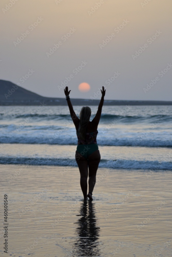 A girl waving to the sun at sunset in Famara