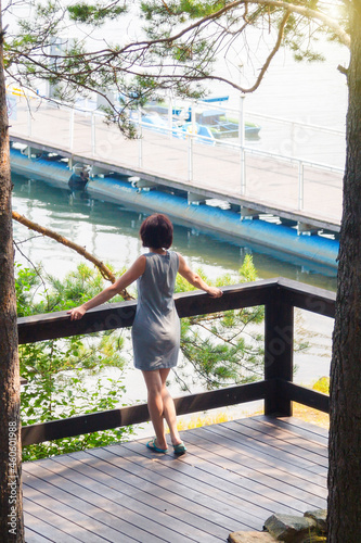 A woman on bridge looks into the distance behind a sailing ship in beautiful green forest.