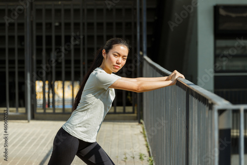 Pretty slim Asian lady in comfortable sportswear leans on bridge handrail at outdoor training on sunny city street side view