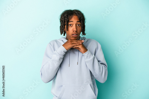 Young african american man isolated on blue background praying for luck, amazed and opening mouth looking to front.