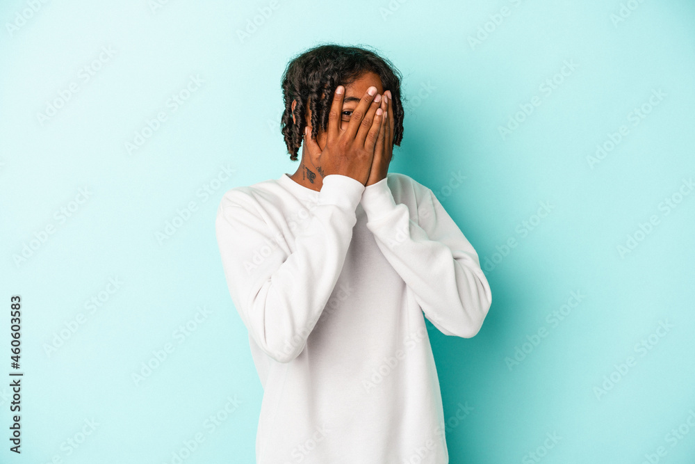 Young african american man isolated on blue background blink through fingers frightened and nervous. Young african american man isolated on blue background blink through fingers frightened and nervous.