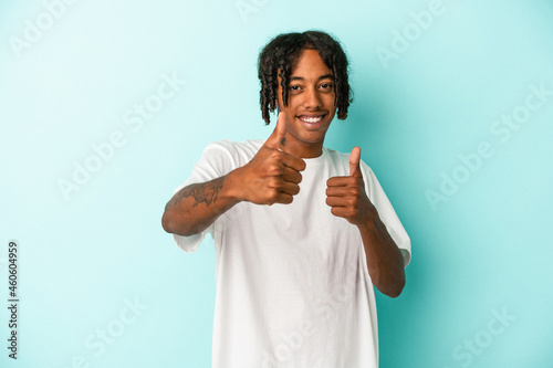 Young african american man isolated on blue background raising both thumbs up, smiling and confident.