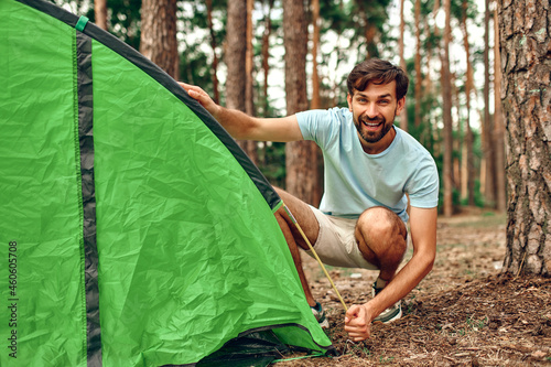 The man went to the weekend and puts up a tent in a pine forest. Camping, recreation, hiking.