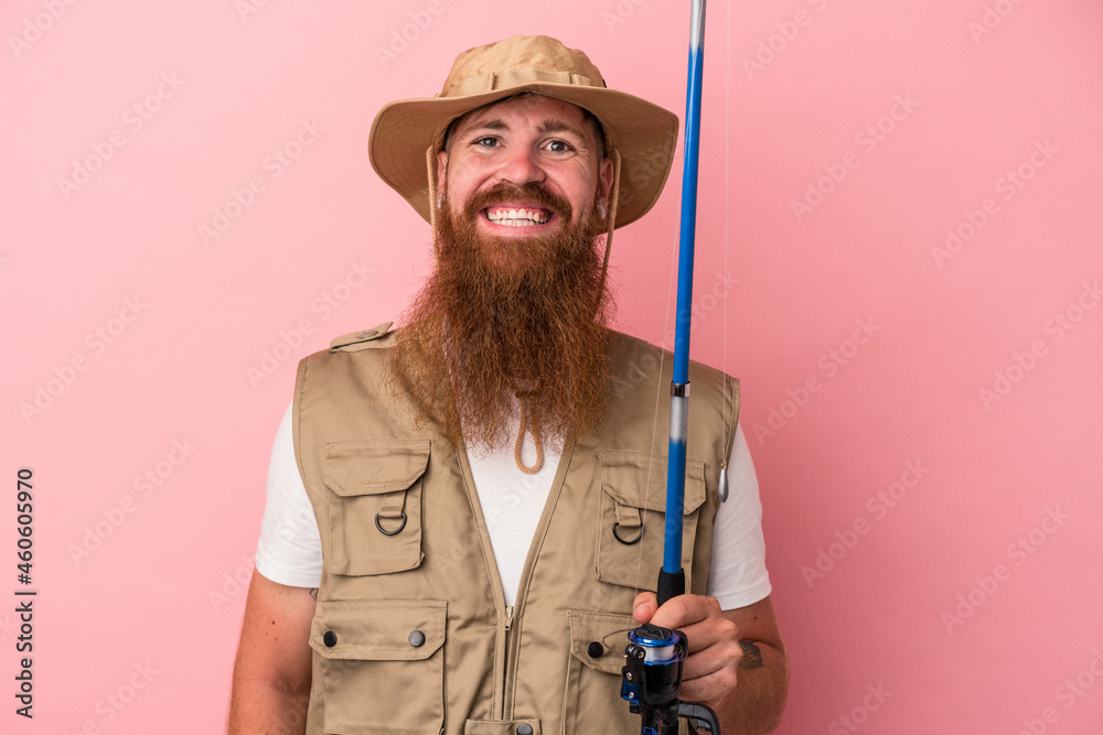Young caucasian ginger fisherman with long beard holding a rod isolated on pink background happy, smiling and cheerful. Young caucasian ginger fisherman with long beard holding a rod isolated on pink background happy, smiling and cheerful.