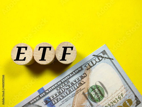 Wooden block cylinder written with text ETF with dollar money on a yellow background.