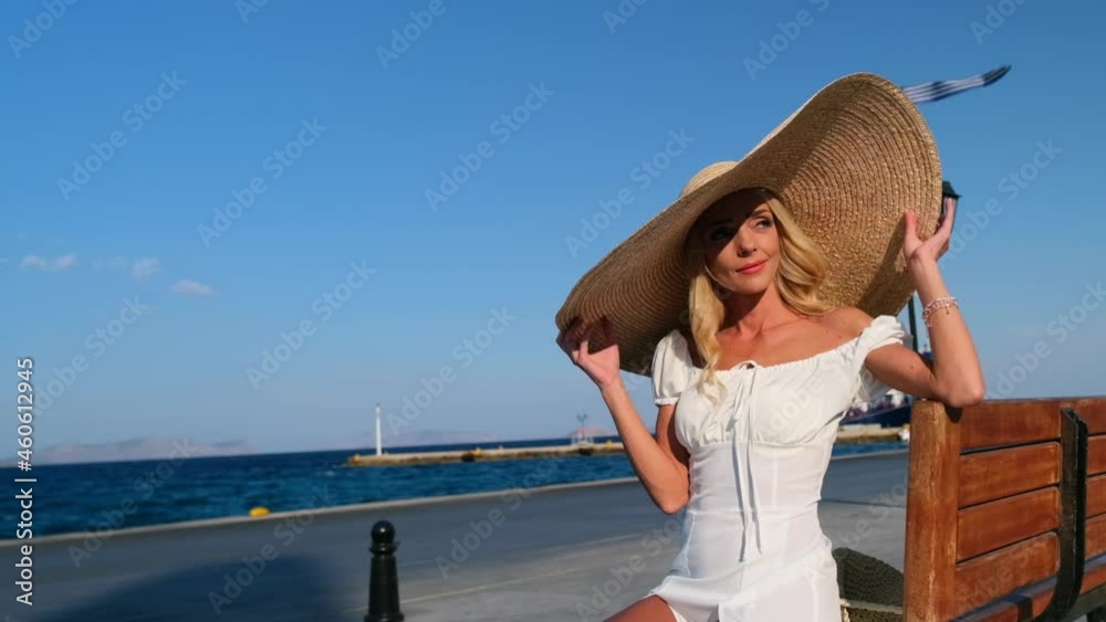 Woman in sun straw hat sitting on a wooden bench on blue sea background at Spetses. Greece Woman in sun straw hat sitting on a wooden bench on blue sea background at Spetses. Greece