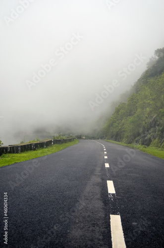 Empty road and dense clouds covering the forest and mountains. Dark clouds on the pitched road pathway