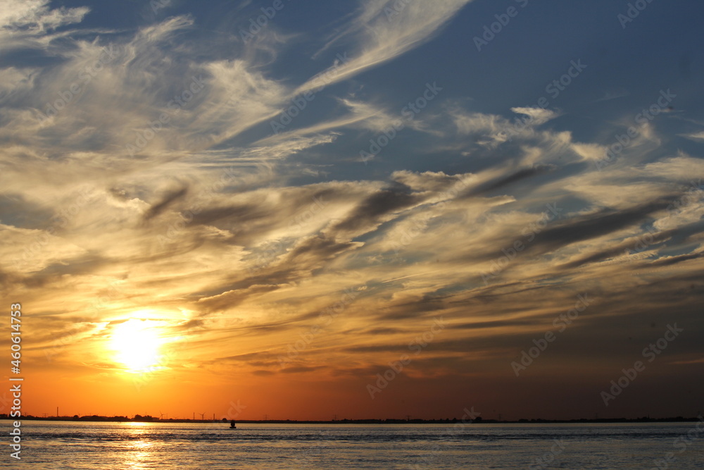 a sunset at the sea at the dutch coast in september with artistic cloud stripes next to the bright sun in the orange and blue sky a sunset at the sea at the dutch coast in september with artistic cloud stripes next to the bright sun in the orange and blue sky