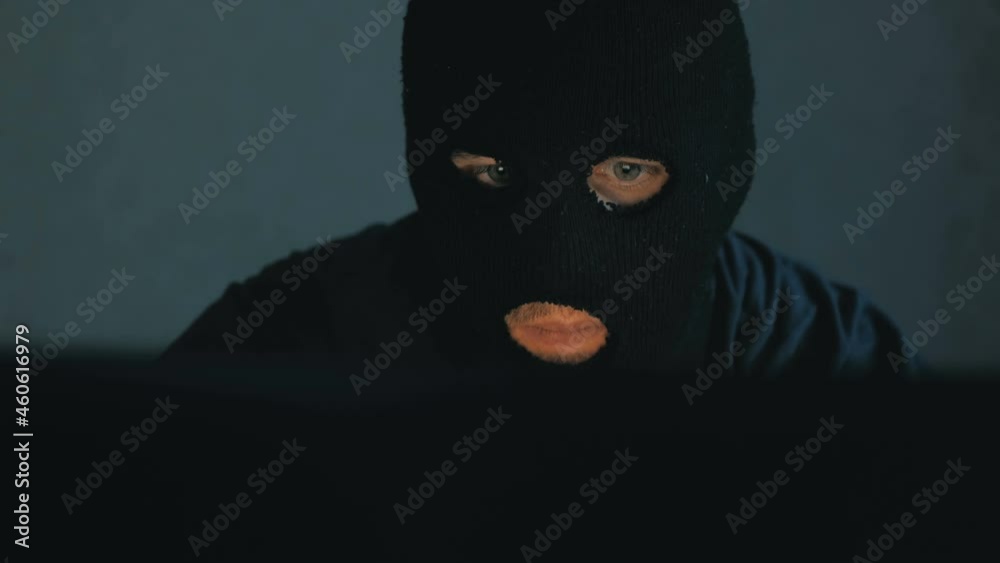 An Internet hacker in a black balaclava sits in a chair and steals data from a laptop. An anonymous hacker in a black hoodie calls his victim on the phone and threatens to crack the database passwords An Internet hacker in a black balaclava sits in a chair and steals data from a laptop. An anonymous hacker in a black hoodie calls his victim on the phone and threatens to crack the database passwords