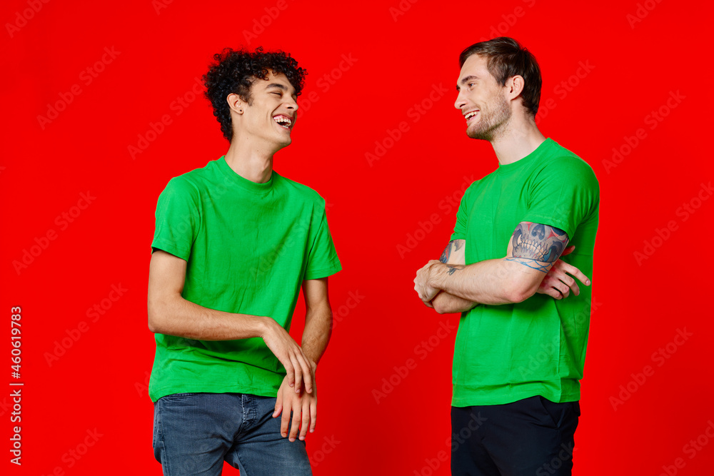 Two cheerful friends in green t-shirts communicating emotions red background