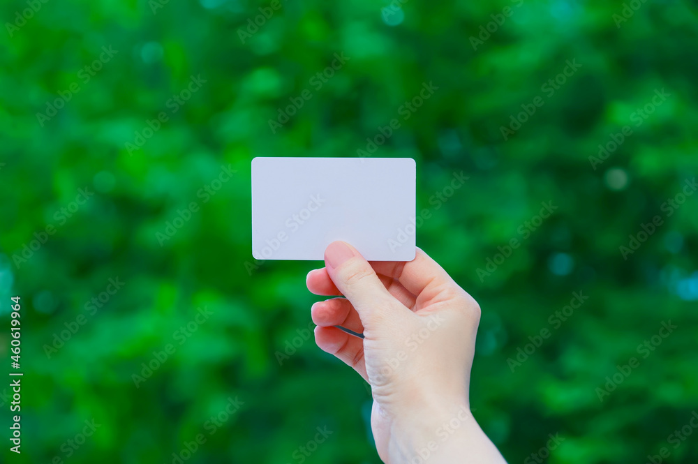 White plastic business card in hand Caucasian woman on background of green foliage. White plastic business card in hand Caucasian woman on background of green foliage.