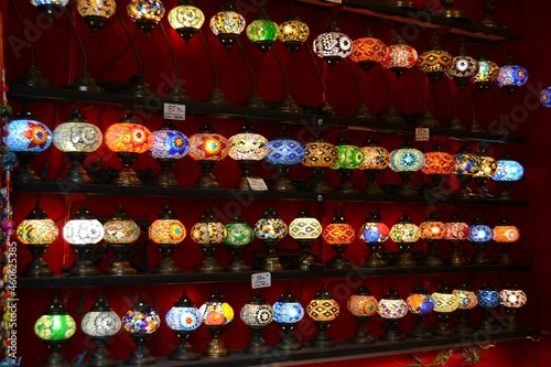 Many colorful turkish,oriental lamps with mosaic patterns on shelves, on dark red wall.