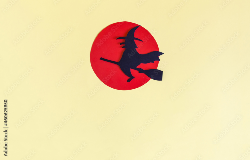 The shadow of a black witch flying on a broomstick against a red moon on a yellow background. A mock-up of an ad for Halloween.